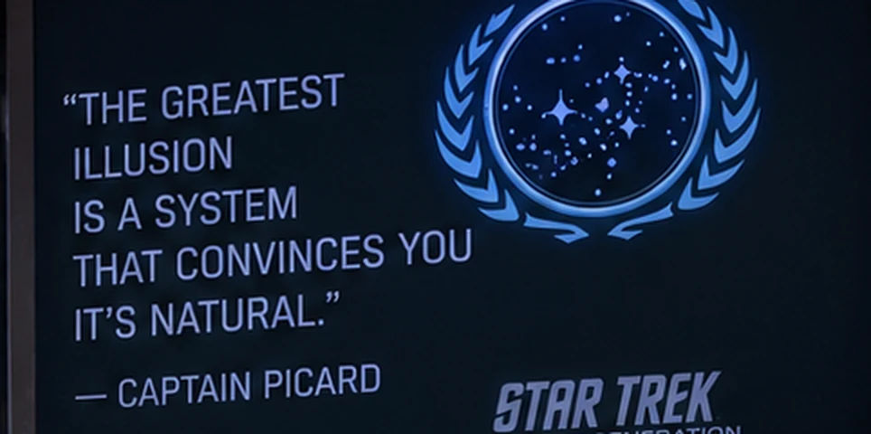 A wall screen showing the line: the greatest illusion is a system that convinces you it's natural.